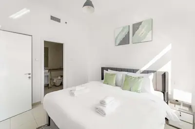 a white bedroom with a large white bed with green pillows at Silkhaus Comfy 1BR in Botanica Tower near Dubai Marina in Dubai