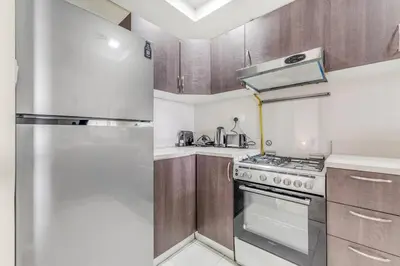 a kitchen with a stainless steel refrigerator and wooden cabinets at Waves - Spacious 1BR with Balcony & Cozy Interiors in JVC in Dubai