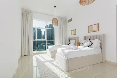 a white bedroom with two beds and a large window at Waterfront flat Stunning view Sleeps 6 in Dubai
