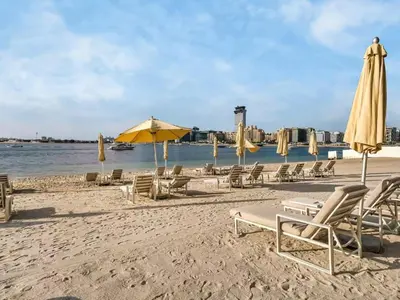 a group of chairs and umbrellas on a beach at Homes Beyond I Stylish 2BR Beachfront Bliss in Dubai