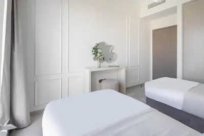 a white bedroom with two beds and a table at Frank Porter - Grande Signature Residences in Dubai