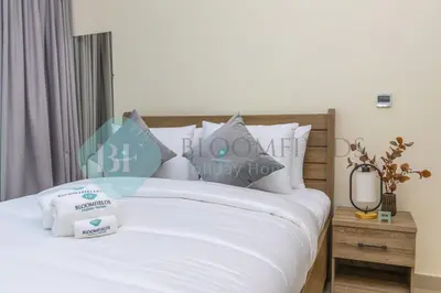 a bedroom with a bed with white sheets and pillows at Bloomfields Cozy Stu Azizi Farhad in Dubai