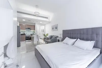 a bedroom with a large white bed and a kitchen at HAVN - Studio Apartment infront of CircleMall, JVC in Dubai