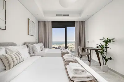 a white hotel room with a bed and a desk at UrbanStays Dubai - Paramount Midtown in Dubai