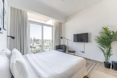 a white bedroom with a large bed and a window at HAVN - New Studio Apartment in Bloom Towers, JVC in Dubai