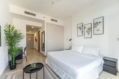 a white bedroom with a large bed and a table at HAVN - New Studio Apartment in Bloom Towers, JVC in Dubai