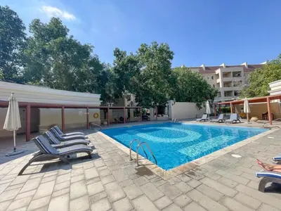 a swimming pool with lounge chairs and a building at Spacious studio in a green oasis in Dubai