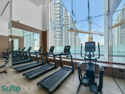 a row of treadmills in a gym with large windows at Perfect Blend of Comfort and Cozy 1 Bedroom in JVC in Dubai