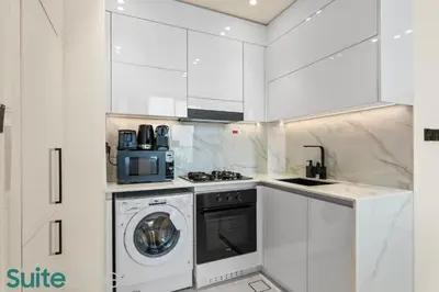 a white kitchen with a washing machine and a microwave at Perfect Blend of Comfort and Cozy 1 Bedroom in JVC in Dubai