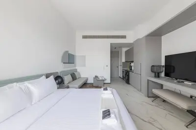 a white bedroom with a large bed and a television at Brand New Studio 15 mins drive from Business Bay in Dubai