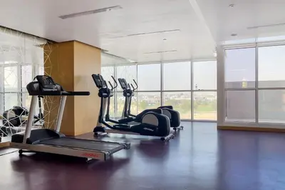 a gym with several tread machines in a room with windows at Modern 1BR apartment Artesia DAMAC Hills in Dubai