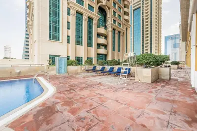a patio with a pool and chairs and a building at Renovated Unit with Skyscraper Views, Close to JBR Beach, Elite Residence, Dubai Marina by Deluxe Holiday Homes in Dubai