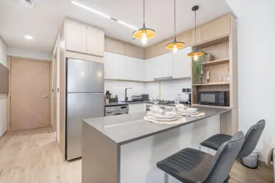 a kitchen with white cabinets and a stainless steel refrigerator at Smartly Designed Studio in JVC in Dubai