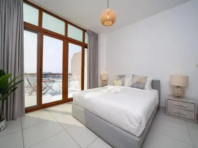 a white bedroom with a large bed and a balcony at Chic Waterfront Studio in Palm Views West in Dubai