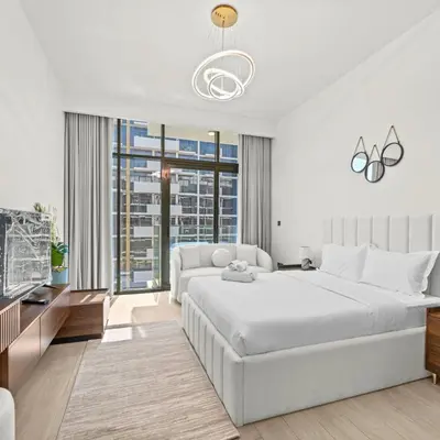 a white bedroom with a large bed and a tv at Azizi Riviera 35 - Studio with full Kitchenet - Ideal for monthly in Dubai