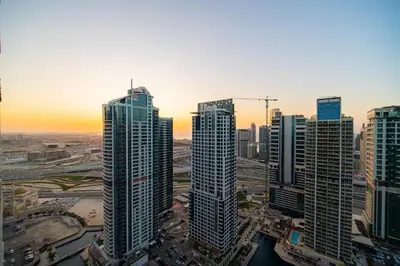 a group of tall buildings in a city at sunset at SettlerHomes - Chic JLT 29 Floor Near Panoramic Lake in Dubai