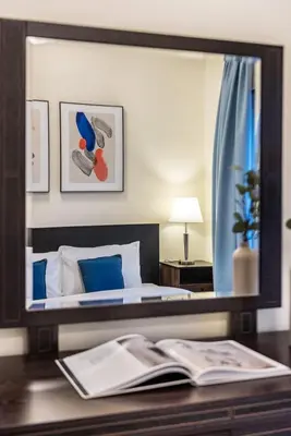 a mirror above a desk with a bed and a book at Spacious 1-BR Opposite Mall with Huge Pool & Gym in Dubai