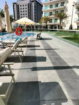 a pool with chairs and umbrellas next to a building at Fully Furnished Elegant Studio Apartment Close by Dubai Science Park, Dubai Miracle Garden, Butterfly Garden and Dubai Hills Mall in Dubai