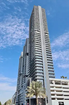 a tall building with a palm tree in front of it at Fully Furnished Cozy Studio at JVC Dubai, Short Drive to Dubai Marina, JBR, Downtown Dubai in Dubai
