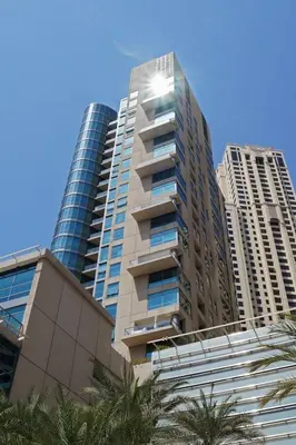 a tall building with palm trees in front of two tall buildings at HAVN - 1 Bed in Dubai Marina, 5mins walk to JBR in Dubai