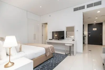 a white bedroom with a bed and a desk and a television at Cozy and elegant Studio in Business Bay in Dubai