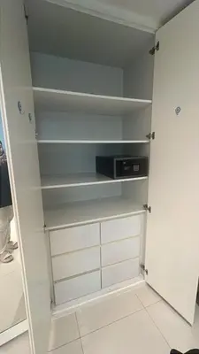 a walk in closet with white shelves and a microwave at Capital bay in Dubai