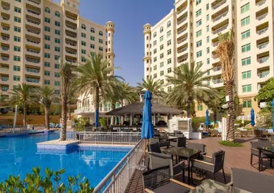 a pool at a resort with tables and umbrellas at Bespoke Holiday Homes - 2BR Apartment with Riva Beach Club Access, Al Nabat in Dubai