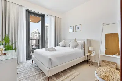 a white bedroom with a bed and a large window at Stylish 1BR with Pool, Gym, BBQ Area & Playground in Dubai