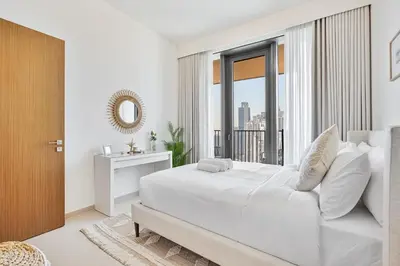 a white bedroom with a large bed and a window at Stylish 1BR with Pool, Gym, BBQ Area & Playground in Dubai