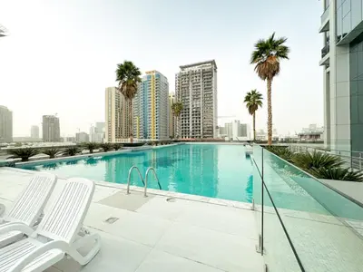 a swimming pool on the roof of a building with palm trees at Modern Studio Living in JVC's Regina Tower in Dubai