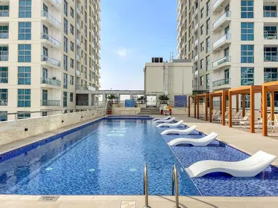 a large swimming pool with white lounge chairs next to buildings at Cozy Studio at DEC Tower in Dubai