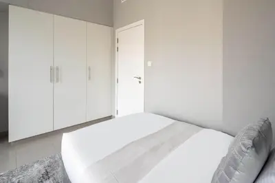 a white bedroom with a bed and white cabinets at Frank Porter - Hayat Boulevard 2B in Dubai
