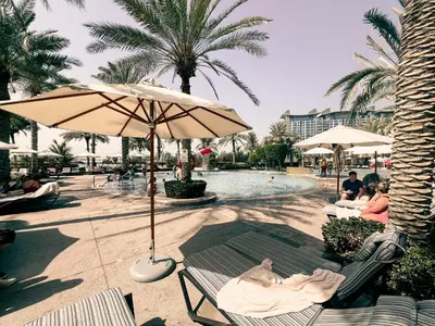 a pool with an umbrella and a person laying on a bench at New Fairmont Residence Private Beach club access Palm Jumeirah in Dubai