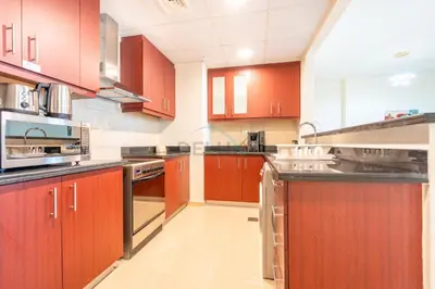 a large kitchen with red cabinets and appliances at Sea-Facing 1BR with Ain Dubai View Close to Marina Beach, Rimal 3, Jumeirah Beach Residence by Deluxe Holiday Homes in Dubai