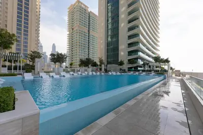 a large swimming pool with chairs and buildings at Luxury 2BR Apt with Pool, Gym & Sea Views in Dubai
