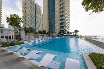a large swimming pool with lounge chairs and buildings at Luxury 2BR Apt with Pool, Gym & Sea Views in Dubai