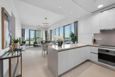 a kitchen with white cabinets and a living room at Magnificent - New 1BR in Canal Front Residences in Dubai
