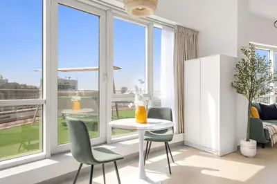 a living room with a table and chairs and windows at Silkhaus Cozy Studio at Madison in Barsha Heights in Dubai