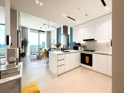 a kitchen with white cabinets and a living room at Trophy-Brandnew Premium and Vibrant 1BR in JVC in Dubai