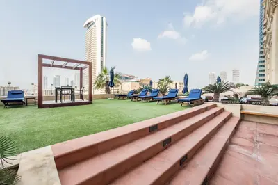 a rooftop patio with chairs and a table and grass at Redesigned High-Rise 1BR Near Key Landmarks, Elite Residence, Dubai Marina by Deluxe Holiday Homes in Dubai