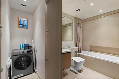 a bathroom with a washing machine and a bath tub at Elegant Creekside 1BR with Panoramic Views in Dubai
