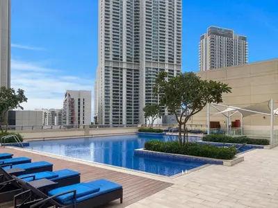 a swimming pool with blue lounge chairs and buildings at Elegant Creekside 1BR with Panoramic Views in Dubai