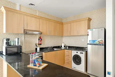 a kitchen with wooden cabinets and a white refrigerator at Silkhaus Homey 2BR at Mayfair Tower in Business Bay in Dubai