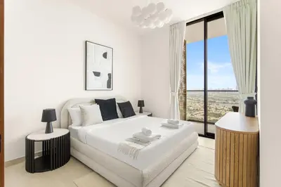 a white bedroom with a bed and a large window at VayK - Luxury 2BR with Jacuzzi in JVC in Dubai