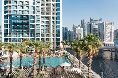 a pool with palm trees in front of a large building at Damac Maison Prive, Lake View - Free Parking in Dubai