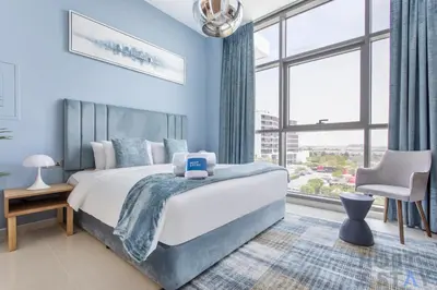 a blue bedroom with a large bed and a chair at Elegant Studio Without Balcony- Damac Hills, Dubai - Host & Stay in Dubai