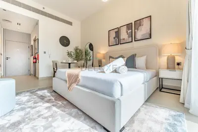 a white bedroom with a large bed and a table at Community Views Studio Near Nad Al Sheba Gardens with Balcony, MAG 980, Mohammad Bin Rashid by Deluxe Holiday Homes in Dubai