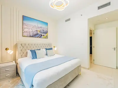 a white bedroom with a large bed with blue pillows at the 'Paris' Condo - Stylish 2Bd with Burj View in Dubai