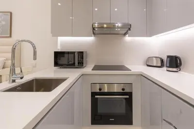 a white kitchen with a sink and a microwave at Stylish Studio 5 min Walk to Mall & Burj Khalifa in Dubai