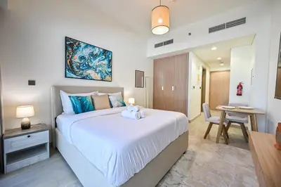 a bedroom with a large white bed and a table at Cozy Studio with Balcony in Azizi Riviera and 10 Mins to Burj Khalifa in Dubai